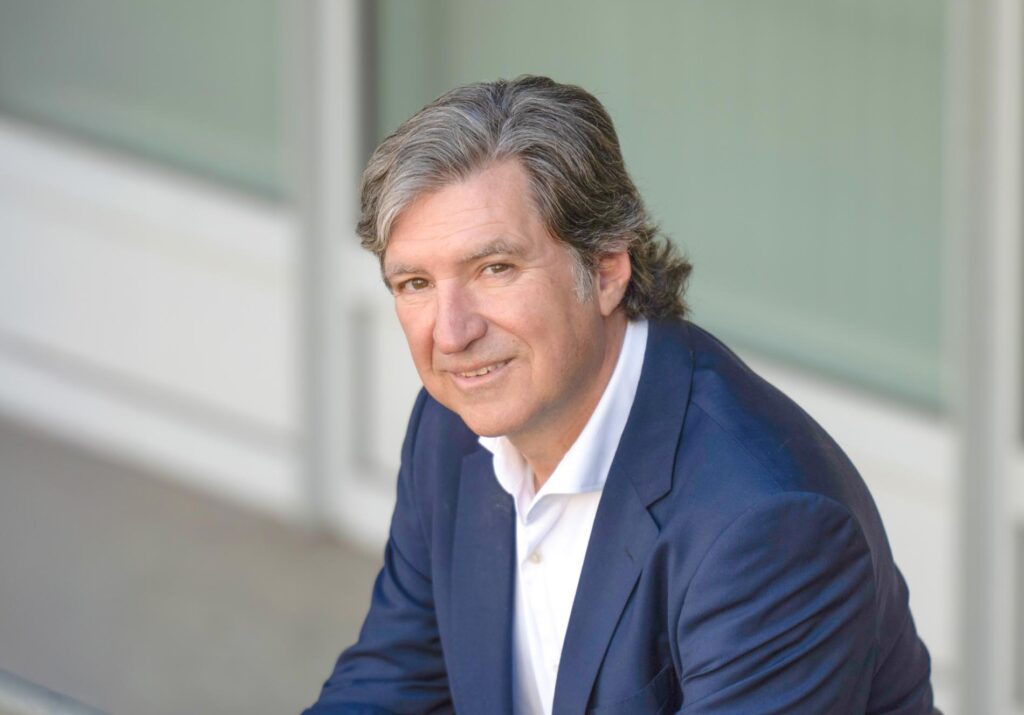 Porträt eines Mannes im dunkelblauen Anzug mit weißem Hemd vor moderner Gebäudefassade.